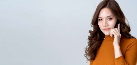 portrait beauty asian woman brown dress smile with happy confident and joyful hand hold smartphone business communication white backgroundの写真素材