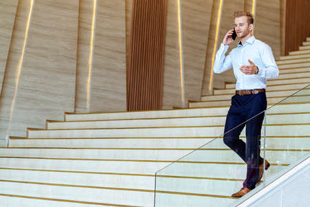 successful smart caucasian businessman walking on stair make communication with smartphone...