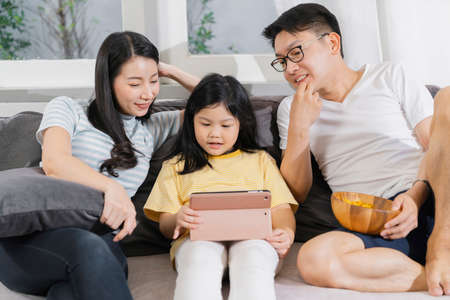 happiness asian family dad mom and daughter sit relax wachting tablet togehter home sweet home conceptの写真素材