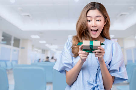 happiness cheerful asian female patient or sick woman in hospital uniform smile and hand hold gift...