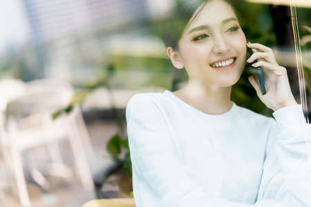 entrepreneur  startup business owner attractive asian female business woman communication with smartphone and laptop white dress cheerful and smile with confience blur office backgroundの写真素材