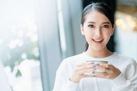 entrepreneur  startup business owner attractive asian female business woman communication with smartphone and laptop white dress cheerful and smile with confience blur office backgroundの写真素材