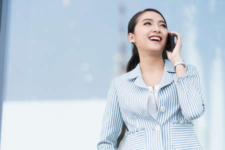 business technology communication ideas concept smart attractive asian woman casual shirt smile and enjoy conversation with smartphone hand gesture with background of modern shop fの写真素材