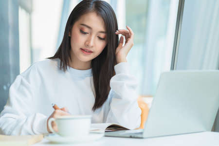 entrepreneur  startup business owner attractive asian female business woman communication with smartphone and laptop white dress cheerful and smile with confience blur office backgの写真素材