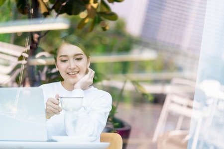 entrepreneur  startup business owner attractive asian female business woman communication with smartphone and laptop white dress cheerful and smile with confience blur office backgの写真素材