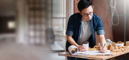 asian attractive glasses interior designer working at house site renovation construction progress with smile and confident at desk with blue print and drawing toolの写真素材