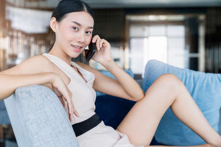 smart attractive beautiful asian female working form home hand use smartphone sit in sosfa couch...