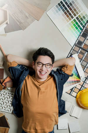 smart happiness asian man house owner laydown on floor with house material sample frame around home...