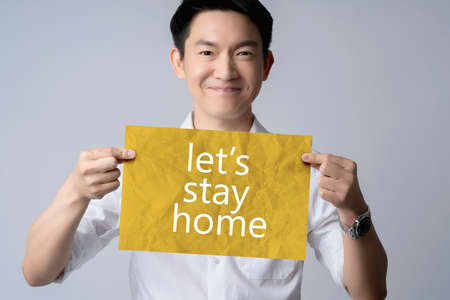 attractive white shirt asian male smile hand hold paper with sentence let stay home in covid-19...