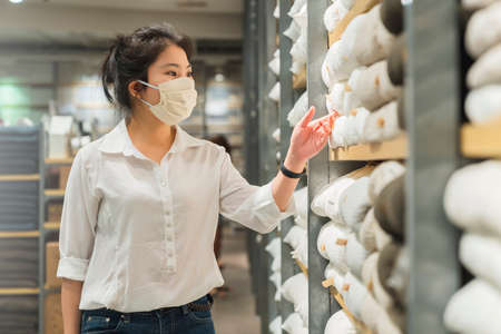 new normal after covid epidemic young smart asian female shopping new lifestyle in storet with face shild or mask protection hand choose consumer products new normal lifestyleの写真素材