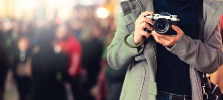 asian female traveller smile happiness hand hold mirrorless camera enjoy nightlife lifestyle tourost with light bokeh and crowd of people blur background in winter season close up banner sizeの写真素材