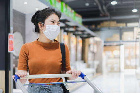 New normal lifestyle asian female brown dress wear protecting mask shopping in department store after lockdown quarantine period New normal lifestyle hand use smartphone bokeh backgroundの写真素材