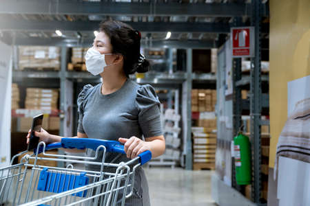 young asian female casual dress  shopping with cart trolley in department store warehouse with new...