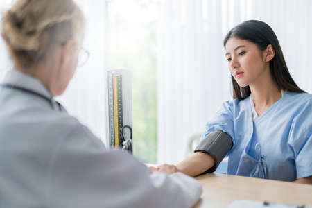 health ideas concept with close up Doctor hand  using sphygmomanometer with stethoscope checking blood pressurefor asian woman patient in the hospital backgroundの写真素材