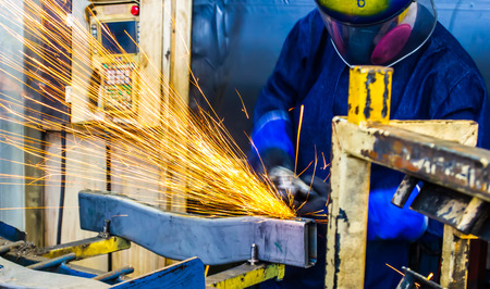 The worker grinding metal in manufacturing plant