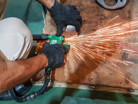 worker grinding metal in manufacturing plant automotive part.