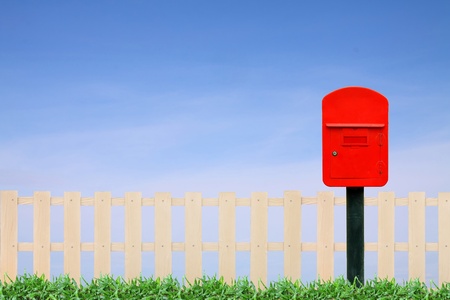 red postbox with white fence and clear blue sky 