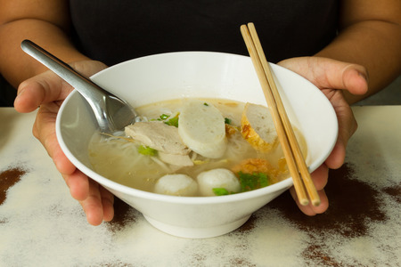 two hand hold a bowl of thai style noodle with clear soup