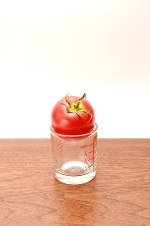 tomato on measuring glasses cup on wooden topの写真素材