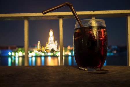 Cool coke glass with tube. On the wood table The atmosphere of arun temple at nightの写真素材