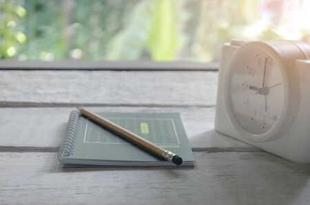 Class room in nature background with Green books, pencils, alarm clock, on a white wooden table with light orangeの写真素材