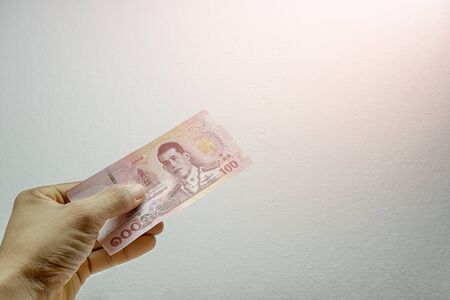 A mans hand is holding one 100 bank notes on a white background. Concept Thai baht currency banknote