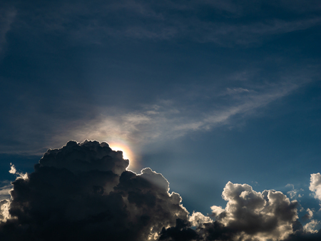 The Fluffy Gray Clouds behind The Sun in The Blue Skyの写真素材