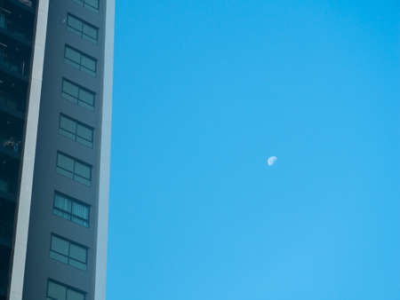 The Moon Appears in The Daytime beside The Modern Building during in the Late Afternoonの写真素材