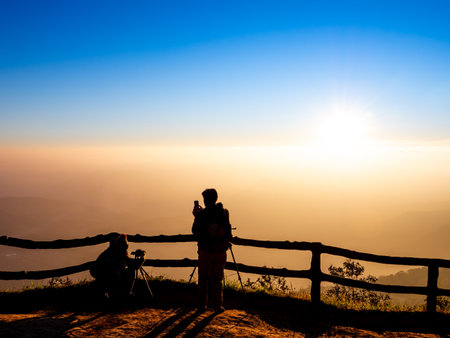 Silhouette of photographer taking photo with sunrise on top of mountain.