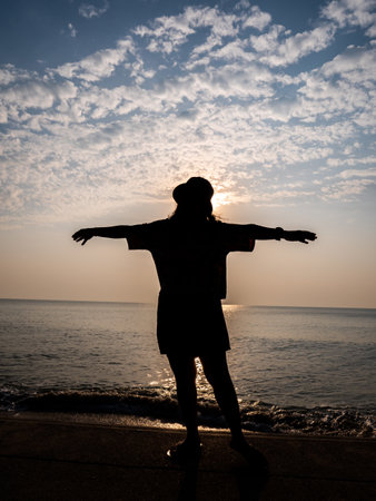 The Silhouette Woman Wearing a Hat Stands with Her Arms Crossed behind The Sun , Sky and Seaの写真素材