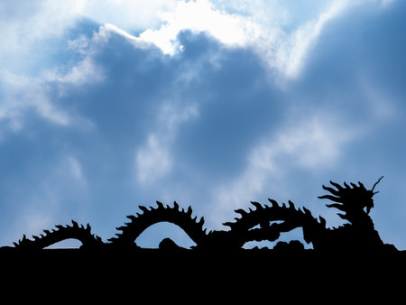 The Silhouette of Dragon Statue Face to The Right Walking on The Roof behind The Sun Light and Blue Skyの写真素材