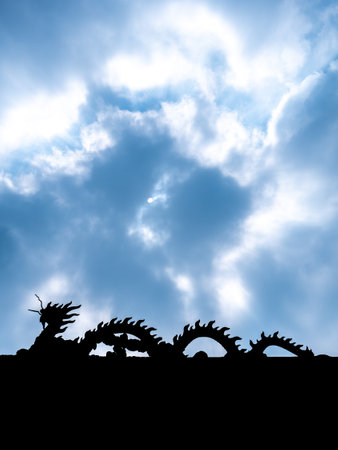 The Silhouette of Dragon Statue Face to The Left Walking on The Roof behind The Sun Light and Blue Skyの写真素材