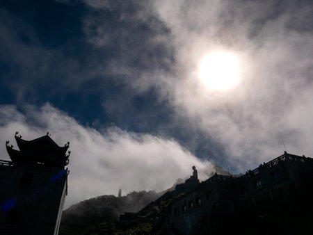 The Silhouette Buddaa Statue Sitting on The Top of The Hill in Thick Fog on Fansipan Mountain in Sapa Vietnam behind The Sunの写真素材
