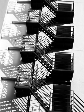 A monochrome study of a fire escape's geometric form against a stark building wall. Light and shadow...