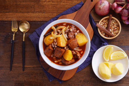 Thai food, pork massaman curry with potatoes, peanuts, coconut milk and onions in a cup on a wooden tableの写真素材