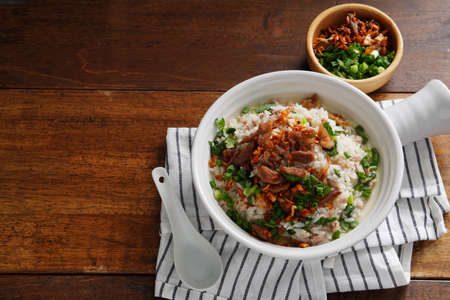 Porridge with spiced pork porridge Garnish with spring onions, coriander, sauteed cabbage, and fried garlic in a baking cup with handle on a wooden table.の写真素材