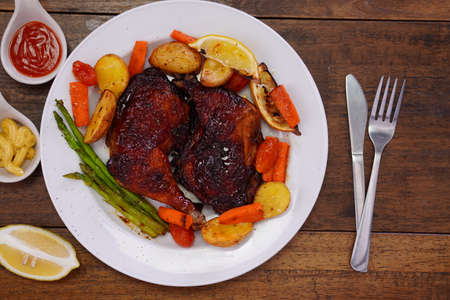 Homemade Baked Chicken Drumstick with Potatoes in a white plate on an old wooden table.の写真素材