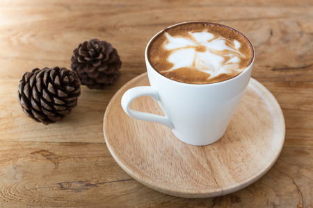 Cup of cappuccino with latte art on a wooden plate and wooded tableの写真素材