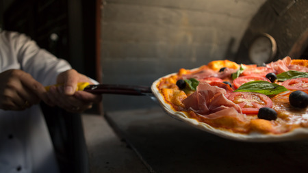 Chef put parma ham pizza in to clay stove at Italian restaurant.