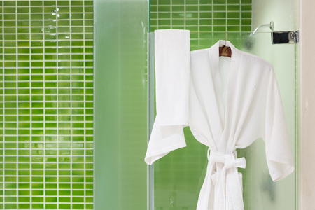 White bathing gowns hanging on glass shower box with green tiles wallの写真素材