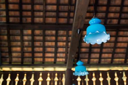 Hanging old lantern and light bulb n Thai house with clay tiles roof in the background.