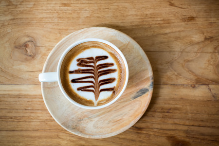 Cup of cappuccino with latte art on a wooden plate and wooded table.の写真素材