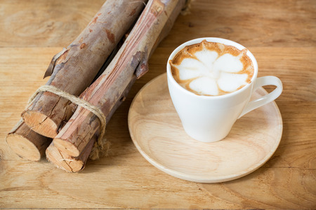 Cup of cappuccino with latte art on a wooden plate and wooded table decorated with dried wood on the side.の写真素材