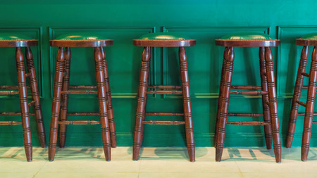 Row of wooden stools in front of green counter inside a vintage style bar.の写真素材