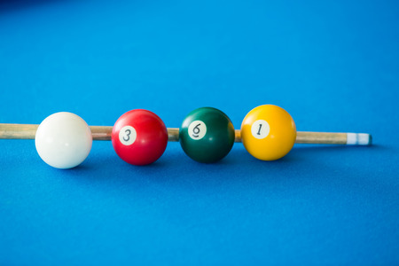 Colorful pool balls and pool stick on a blue table.