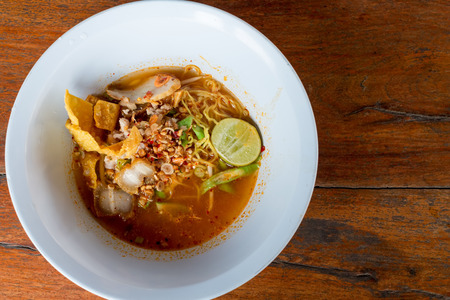 Egg noodle with tom yum soup in white bowl on wooden table.の写真素材