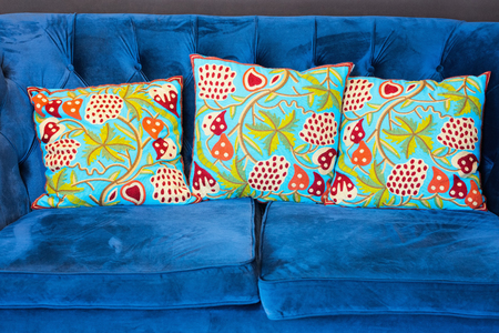 Green indian style cushions on a blue velvet sofa.