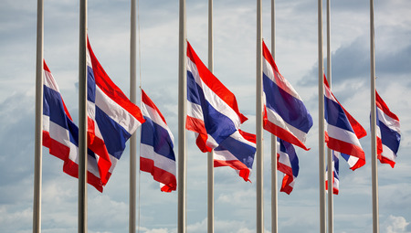 Half staff Thai flags against cloudy sky.