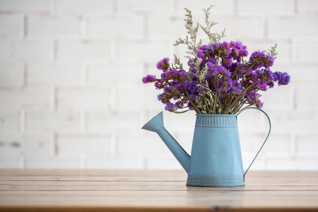 Violet dried flowers in blue tin watering flower pot on wooden table with white brick wall background.の写真素材