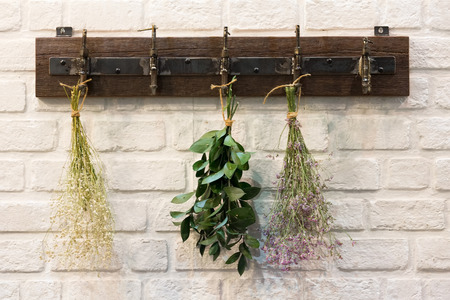Wooden vintage style Hanger / Hooks  on white brick wall decorated with dried bouquets in a country style home.の写真素材